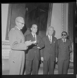 Fotografia "Entrega de Espadim ao representante do embaixador dos EUA. Sr. Mean Gordon representante do embaixador Linconl Gordon, recebe das mães do Cel. Gustavo Borges, espadim oferecido pelo Cel. Edson Moura Freitas, comandante da Polícia Militar, Reportagem de Nelson Silva" ([Local n/d] , 1963) [negativo]. / Fotógrafo(a): Méra.  -- ITEM-0001.