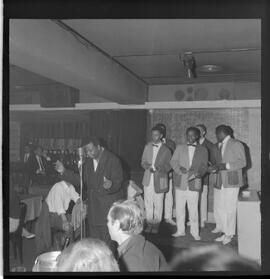 Fotografia "RONDA DAS BUATES [BOITES]; 'RONDA DAS BOITES' ' BOITE AU BON GOUUMET [GOURMET]' 'Ronda das Buartes [Boates]' (Apresentação de Monsueto e suas pastoras), Reportagem de Eli" ([Local n/d] , 1963) [negativo]. / Fotógrafo(a): Roberto.  -- ITEM-0006.