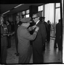 Fotografia "BRASÍLIA - Ministro da Marinha entrega condecorações (medalha do Mérito Naval) à diversas personalidades (Helio de Almeida pelo ministro Silvio Mota) e outros personagens; MEDALHA DO MÉRITO BSB" ([Local n/d] , 1963) [negativo]. / Fotógrafo(a): Neville.  -- ITEM-0003.