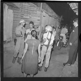 Fotografia "Blitz Policial na Favela do Esqueleto c/ [Duarte]; 'BATIDAS POLICIAIS' 'Blitz' Policial na Favela de Esqueleto, no Maracanã, Reportagem de Duarte" ([Local n/d] , 1963) [negativo]. / Fotógrafo(a): José Gomes; Gomes.  -- ITEM-0011.