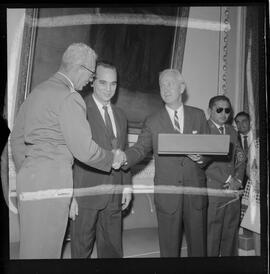 Fotografia "Entrega de Espadim ao representante do embaixador dos EUA. Sr. Mean Gordon representante do embaixador Linconl Gordon, recebe das mães do Cel. Gustavo Borges, espadim oferecido pelo Cel. Edson Moura Freitas, comandante da Polícia Militar, Reportagem de Nelson Silva" ([Local n/d] , 1963) [negativo]. / Fotógrafo(a): Méra.  -- ITEM-0004.